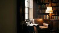 Cozy reading corner with vintage leather armchair and warm lamp light in classic home library with wooden bookshelves for interior design and lifestyle concepts.