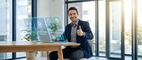 Confident businessman giving thumbs up while working with financial charts and data analytics on laptop in modern office environment.