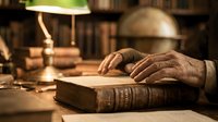 Elderly hands resting on vintage leather-bound book in warm library setting with lamp light. Academic research, wisdom, knowledge concept for education materials.