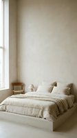 Minimalist bedroom interior with neutral tones, featuring a low platform bed with cream linens, wooden nightstand, and natural light from window for home decor.