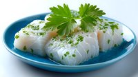 Fresh white fish fillets with green herbs on blue plate ready for cooking or healthy meal preparation.