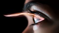 Dramatic close-up of human eye with glowing orange light streak reflection creating futuristic effect against dark background, capturing mystery and technology concept.