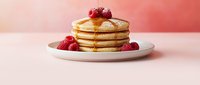 Stack of golden pancakes topped with fresh raspberries and maple syrup on white plate against soft pink background for breakfast menu design.