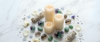Spa wellness arrangement with burning candles, healing crystals, sage bundles and dried flowers on white marble surface for meditation and relaxation rituals.