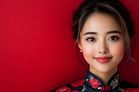 Young Asian woman wearing traditional red floral qipao dress smiling against red background, elegant makeup and updo hairstyle for formal occasions.