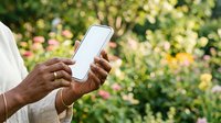 Person holding smartphone with blank screen outdoors in garden with colorful flowers, ideal for app mockups, mobile technology marketing, and digital communication concepts.
