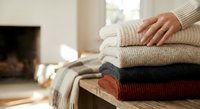 Cozy knitted sweaters stacked on wooden surface near fireplace creating warm autumn winter home comfort atmosphere for seasonal fashion storage.