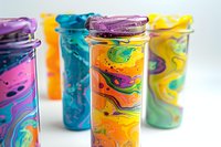 Vibrant swirled paint pattern on colorful travel tumblers with lids arranged in row showing abstract marble design effect on stainless steel cups against white background.