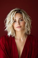 Young Caucasian woman with tousled blonde bob hairstyle wearing deep red blouse against burgundy background, natural makeup and subtle smile creating elegant portrait.