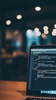 Laptop displaying programming code on screen in modern office environment with warm bokeh lights creating atmospheric workspace ambiance for developers.