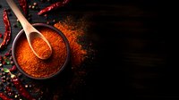 Red chili powder in wooden spoon over dark bowl with scattered spices and dried chilies on black rustic background, dramatic food photography with copy space.