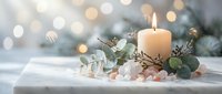 Elegant holiday candle arrangement with eucalyptus leaves and decorative elements on white surface with warm bokeh lights creating festive atmosphere.