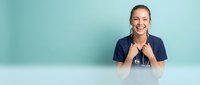 Happy female healthcare professional nurse in navy scrubs with stethoscope smiling warmly against turquoise background for medical marketing materials.