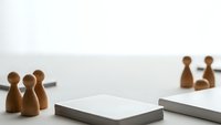 Wooden pawn figures representing team members positioned around notebooks on white desk for business planning and strategy meetings.