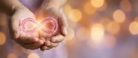 Hands holding glowing infinity symbol with warm bokeh lights background representing endless possibilities, eternal love, and spiritual energy concepts.