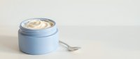 Opened light blue cosmetic jar with cream and small silver spoon on white background, ready for skincare, beauty product packaging, and cosmetics design use.
