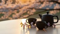 Black ceramic tea set with teapot and cups on wooden table during cherry blossom season at sunset creating warm peaceful atmosphere for relaxation.
