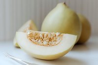 Fresh honeydew melon slice with seeds on white background, showing juicy flesh and whole melons. Appetizing summer fruit for healthy eating and food design.