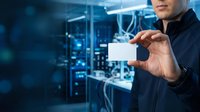 Professional man in dark business attire holding blank white card with digital network interface and server room background, representing technology solutions and corporate networking.