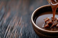 Melted chocolate pouring into ceramic bowl with chocolate pieces on dark wooden surface for dessert preparation and confectionery cooking projects.