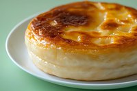 Creamy baked cheesecake with caramelized golden brown top surface served on white plate against mint green background, showing rich texture and layers.
