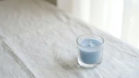 Blue scented candle in clear glass holder on white wooden surface creating peaceful ambiance for relaxation and home decor.