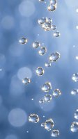 Crystal clear water bubbles floating against soft blue bokeh background with sparkling light reflections creating dreamy aquatic atmosphere for wellness concepts.