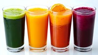 Fresh colorful smoothies in tall glasses - green vegetable, mango, carrot orange, and beetroot purple drinks arranged in row on white background.