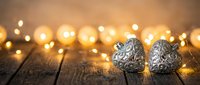 Silver decorative Christmas ornaments with intricate patterns on rustic wooden surface surrounded by warm golden bokeh lights creating festive holiday atmosphere.