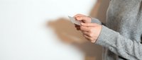 Woman in gray sweater holding smartphone with both hands against white background, cropped view of hands and device for technology and communication concepts.