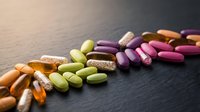 Colorful vitamin and supplement pills scattered on dark surface for health and wellness nutrition concepts.