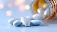 Pills spilling from prescription bottle on soft blue background with bokeh lights, medical concept showing white and blue pharmaceutical tablets.