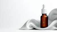 Amber glass dropper bottle with essential oil or serum on white silk fabric background with soft waves and shadows, luxury cosmetic product photography.