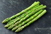 Fresh green asparagus spears arranged on dark slate background. Raw seasonal vegetables with tender tips and thick stalks for healthy cooking and food design.
