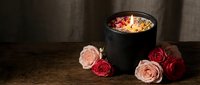 Romantic candle burning in black holder with pink and red roses on rustic wooden table creating warm intimate atmosphere for spa relaxation or date night.