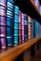 Row of vintage leather-bound books in various colors on wooden library shelf, with selective focus creating depth and bokeh effect. Suitable for education and literature themes.