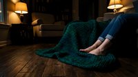 Cozy evening at home with bare feet under soft teal knitted blanket on wooden floor, warm lamp lighting creating relaxing atmosphere for comfort and hygiene.
