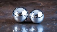 Shiny chrome spheres on dark textured surface with reflection. Metallic balls create minimalist composition with mirror effect and dramatic lighting.