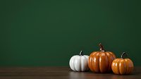 Autumn pumpkins and white squash arranged on wooden surface against green background for fall seasonal designs and harvest celebrations.