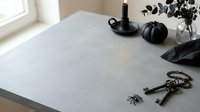Minimalist Halloween table setting with black candle holder, pumpkin, skeleton key chain, spider decorations and dried foliage on white surface.