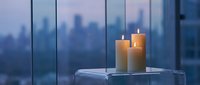 Burning candles on glass table near window with blurred city skyline at dusk creating peaceful ambiance for relaxation and meditation in modern interior.