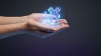 Hands holding glowing holographic puzzle pieces floating above palms representing problem solving and innovation in business technology concepts.