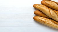 Fresh crusty French baguettes on white wooden background with copy space. Traditional artisanal bread composition for bakery or food service design.