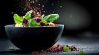 Fresh green basil leaves in black ceramic bowl with scattered spices and herbs on dark background, dramatic food photography with copy space.