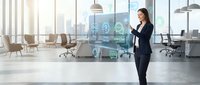 Professional businesswoman using digital interface technology in modern corporate office environment with futuristic holographic display elements.
