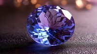 Oval cut tanzanite gemstone with brilliant facets on dark textured surface, illuminated by soft lighting creating purple and blue reflections and bokeh effect.