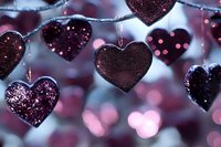 Sparkling burgundy heart-shaped decorations on string lights create romantic atmosphere with soft bokeh background for Valentine's Day celebrations.