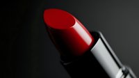 Red lipstick close-up on dark background with dramatic lighting and selective focus highlighting glossy texture and rich crimson color for beauty and cosmetics.
