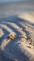 Close-up of sandy beach texture with golden grains and rippled patterns in shallow focus, suitable for travel, nature, and summer vacation backgrounds.