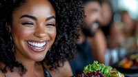 Young African American woman with natural curly hair and bright smile enjoying dinner party with friends, social gathering and celebration atmosphere.